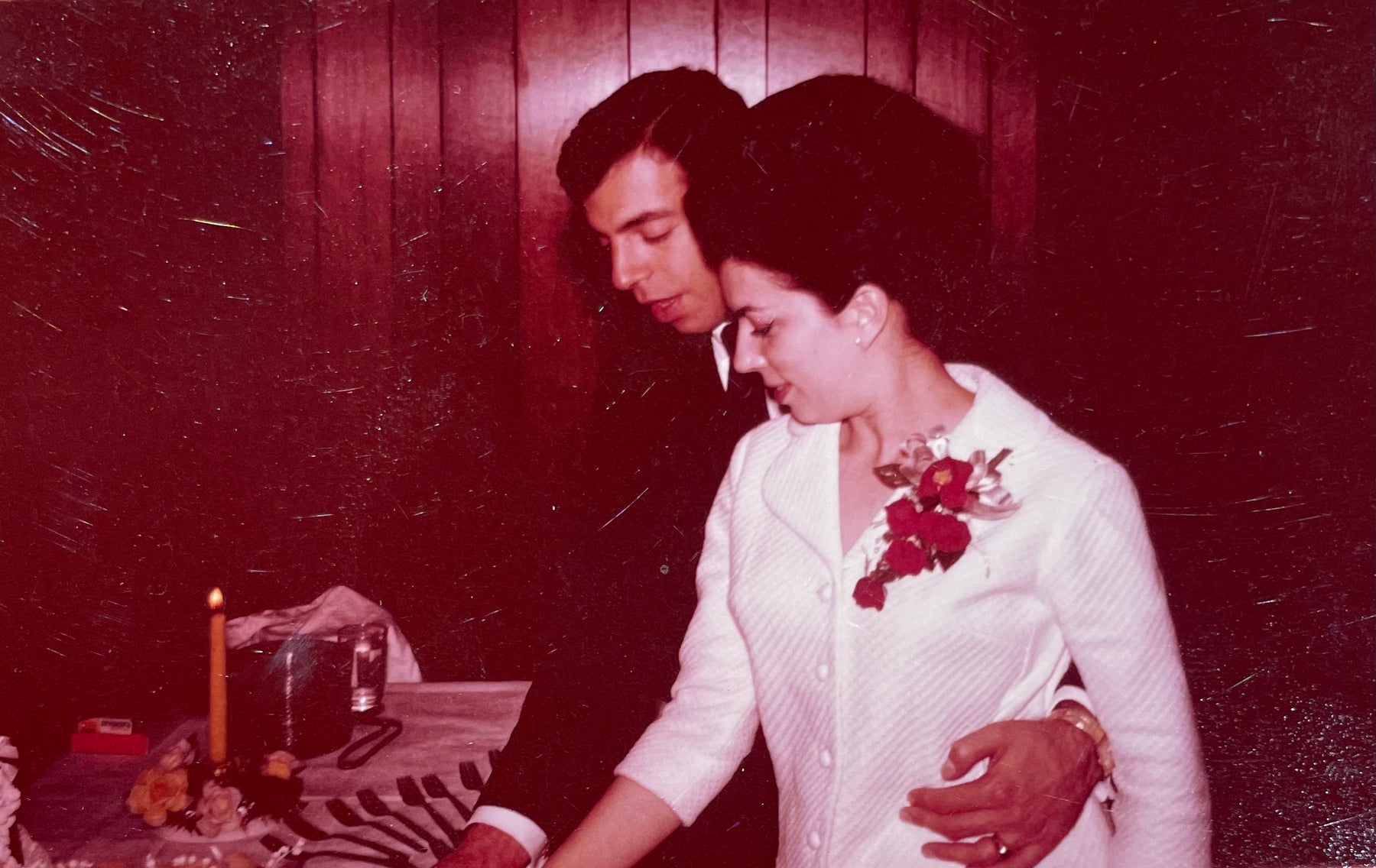 Mom in white jacket with red flowers cutting wedding cake with Dad