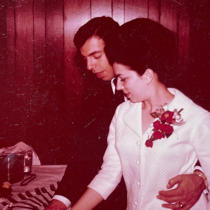 Mom in white jacket with red flowers cutting wedding cake with Dad